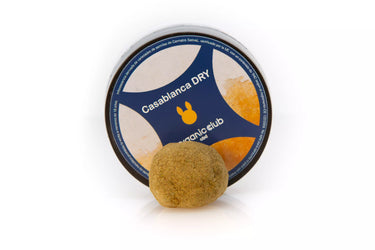 Bola de hachís de CBD anaranjada, con su envase circular detrás